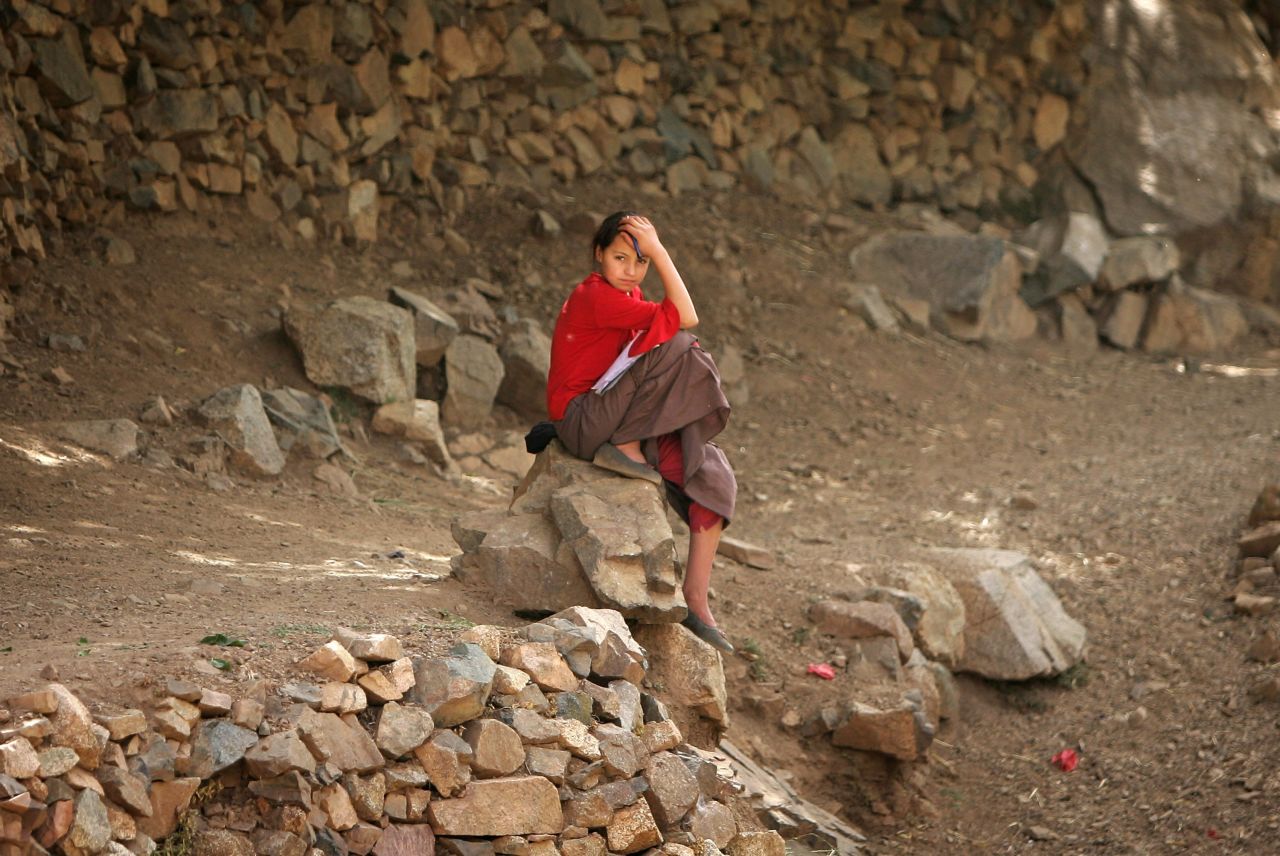 A young Berber girl looks up whilst doing her homework on a rock in the village of Ikkiss, near Imlil, Morocco. She attends school, but usually, young Berber girls living in the Atlas range are put to work at an early age.