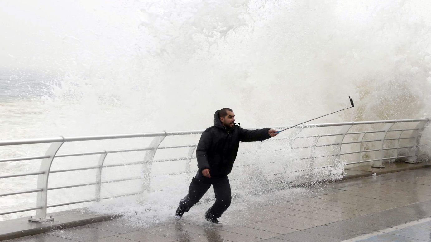 A man uses a selfie stick as a wave crashes behind him Wednesday, February 11, at a seaside promenade in Beirut, Lebanon.