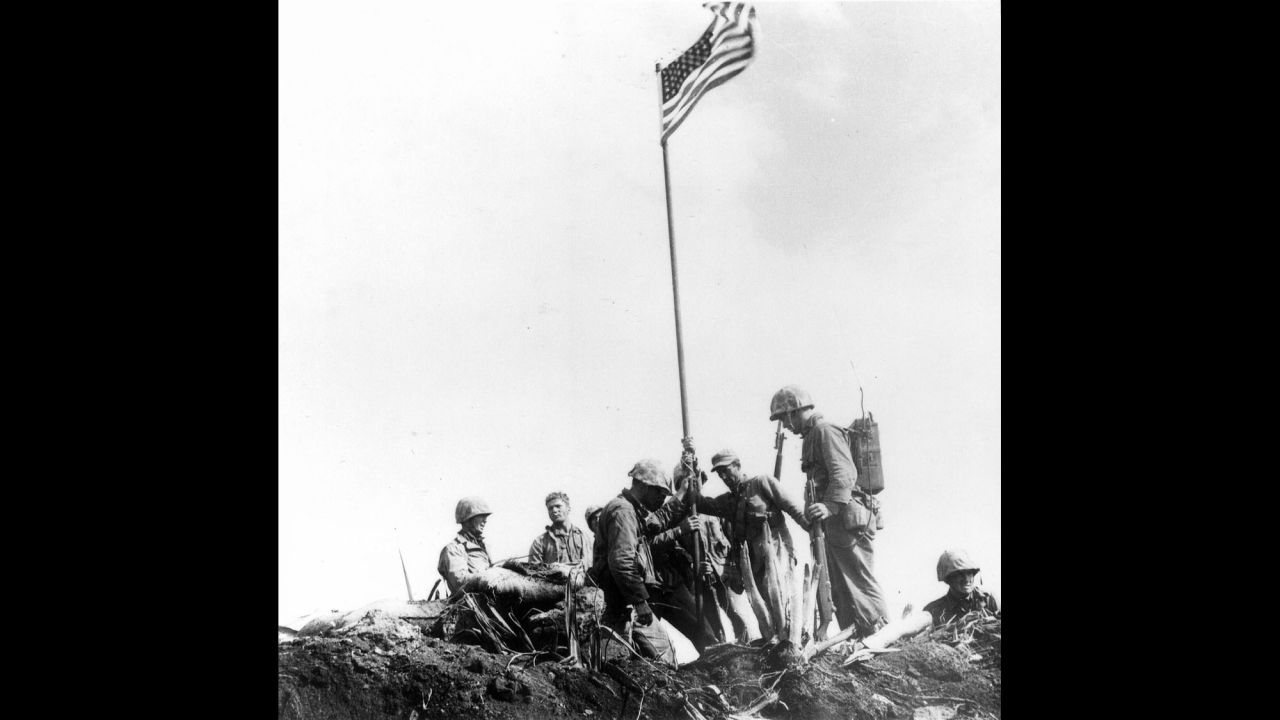 After the first flag-raising, Marines stand near Old Glory as it waves in the wind. 