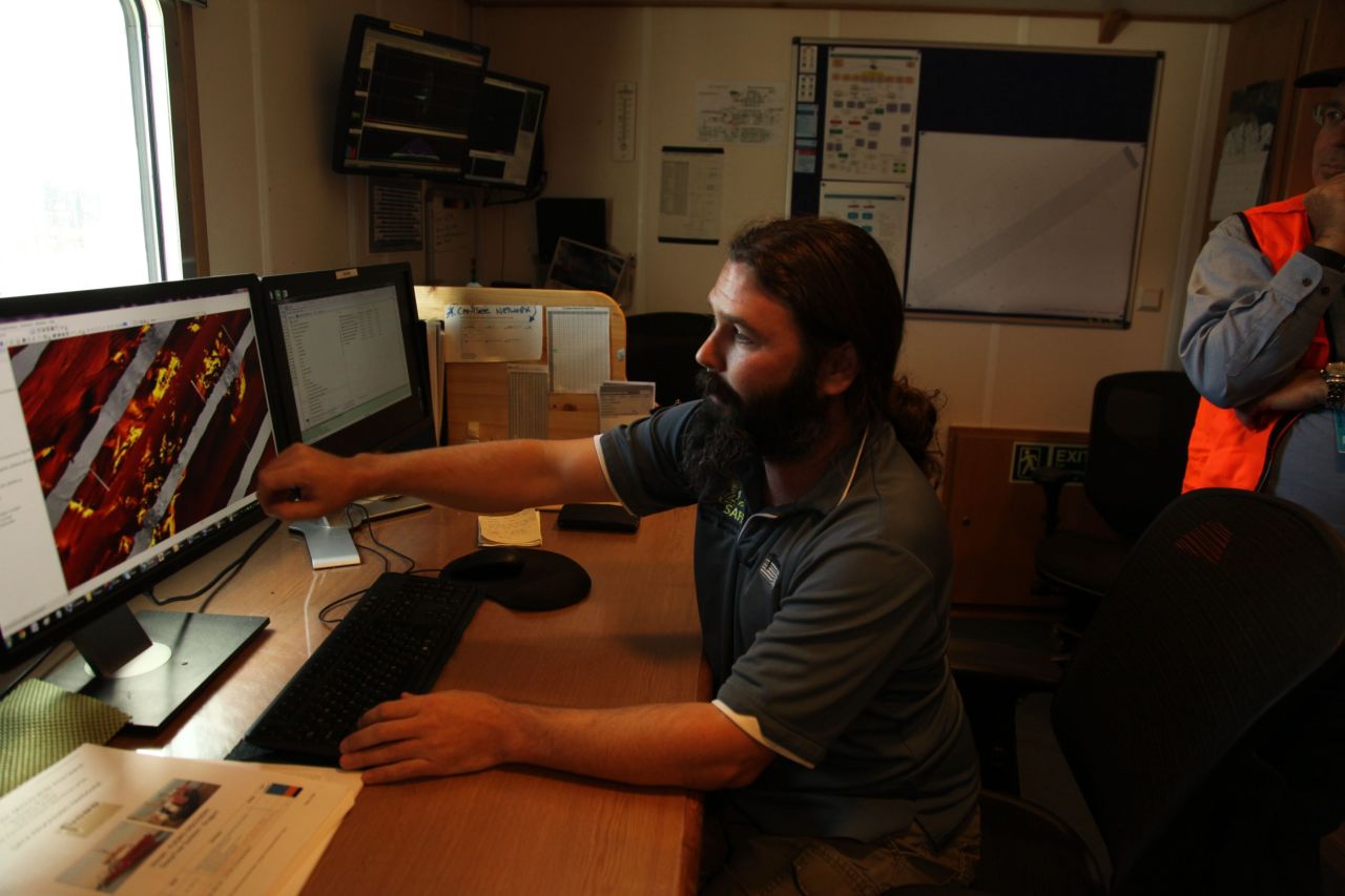 Data supervisor James Kent explains how the side sensor tow fish drawn behind the ship systematically searches in the ocean floor with its side scan sonar towfish, "flying" four kilometers deep, only a hundred meters above the sea bed towed by the Discovery on the end of a ten kilometer long cable.