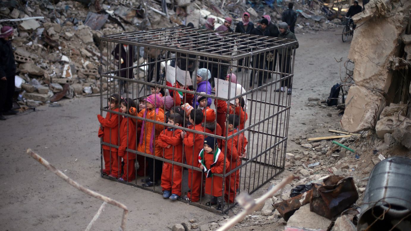 Children in Douma, Syria, carry banners inside a cage on Sunday, February 15, during a protest against forces loyal to Syrian President Bashar al-Assad. The children wore orange jumpsuits, like those worn by victims of the ISIS militant group, as the protest compared al-Assad loyalists to ISIS.