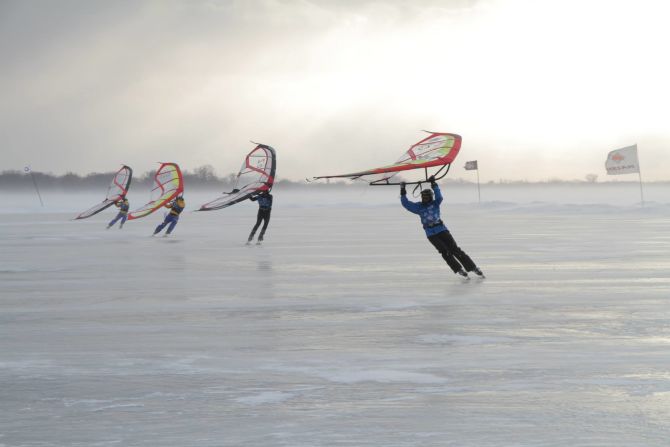The competition includes three classes: sled, kite, and wings. Here, kitewingers carve across the frozen lake. 