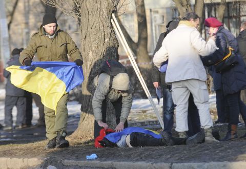 A man holds a Ukrainian flag as he covers a victim of an explosion in Kharkiv, Ukraine, on Sunday, February 22. The explosion during a peaceful protest left two dead and 15 wounded. 