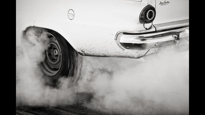 Smoke rises from around the tires of a vintage car at the show. 