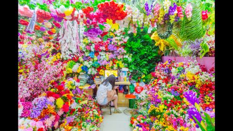 A seller sits among artificial flowers in one of the booths at Commodity City.