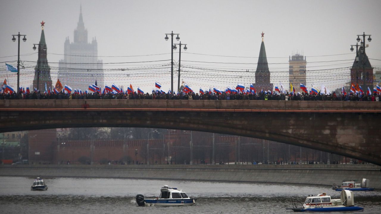 Watched by police in boats on the Moskva River, crowds march across a bridge in Moscow on March 1.