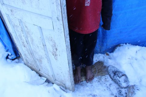 Seven-year-old Khalil stands barefoot on broom bristles in the snow at the entrance of his family's tent in Dikmen Valley, Turkey.  Khalil, a refugee from Aleppo, Syria, does not attend school. "I don't want to go to school. I will work," he said.