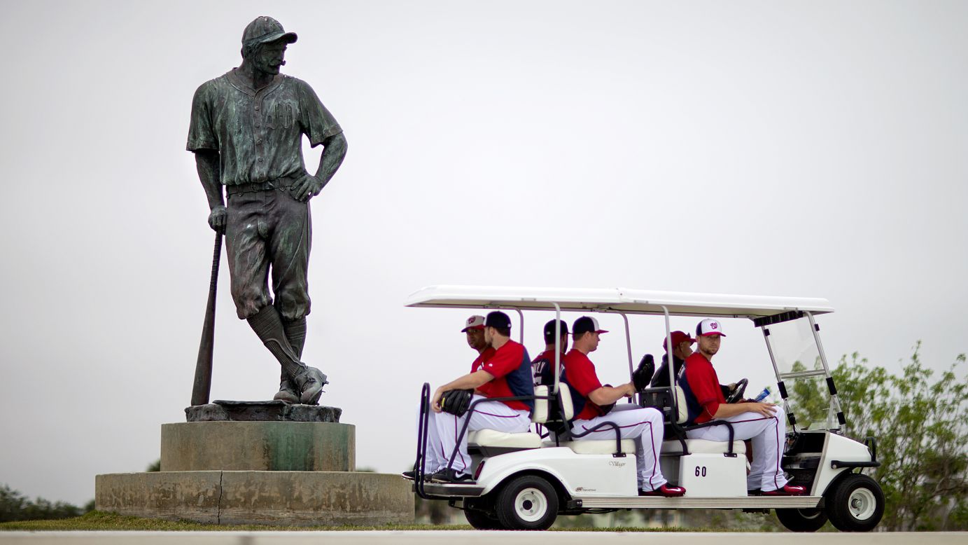 Members of the Washington Nationals ride a golf cart past a "Casey at the Bat" statue on their way to spring training practice Wednesday, February 25, in Viera, Florida.