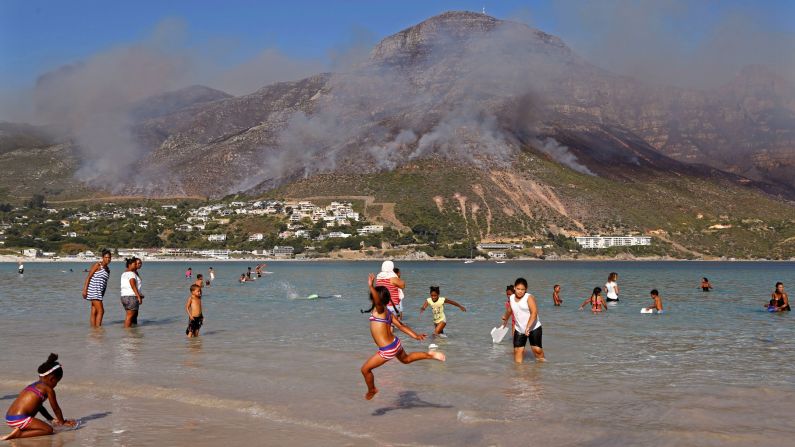 Children swim as the remainder of a fire burns out at Hout Bay, on the outskirts of Cape Town, South Africa, on Tuesday, March 3. South African firefighters say they are battling to control a wildfire that has burned homes in Cape Town's southern peninsula.