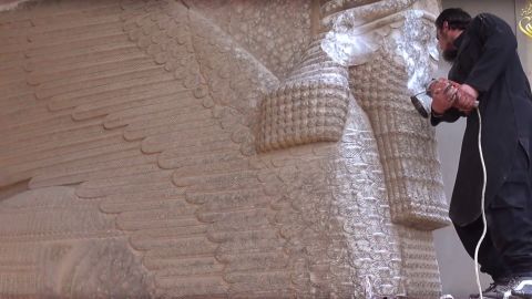 In this image made from video posted on a social media account affiliated with ISIS, a militant uses a power tool to destroy a winged-bull Assyrian protective deity at the Nineveh Museum in Mosul, Iraq. 