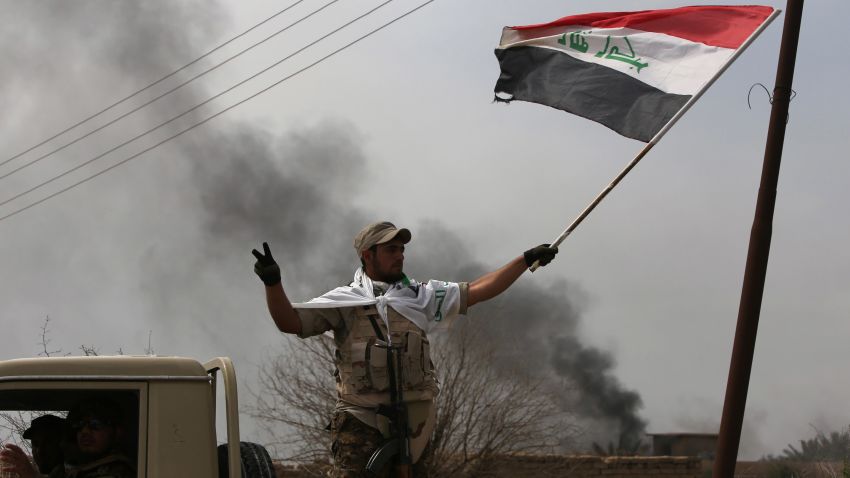 Smoke billows in the background as a member of the Iraqi paramilitary Popular Mobilisation units flashes the "V" for victory sign after regaining control of the village of Albu Ajil, near the city of Tikrit, from jihadists of the Islamic State (IS) group, on March 9, 2015. Some 30,000 Iraqi soldiers, police and the increasingly influential paramilitary Popular Mobilisation units, which are dominated by Shiite militias, have been involved in a week-old operation to recapture Tikrit, one of the jihadists' main hubs since they overran large parts of Iraq nine months ago.  AFP PHOTO / AHMAD AL-RUBAYE        (Photo credit should read AHMAD AL-RUBAYE/AFP/Getty Images)