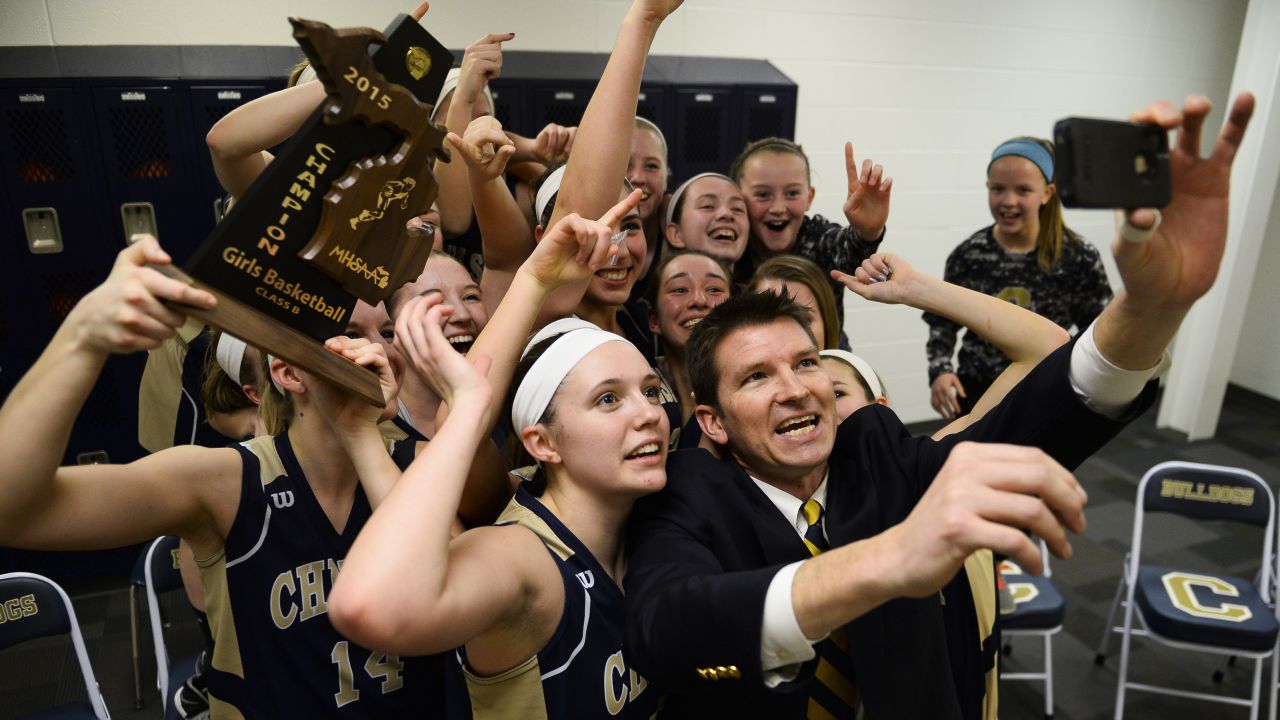Todd Blomquist, head coach of the Chelsea High School girls basketball team, takes a selfie with the team after winning the district championship Friday, March 6, in Chelsea, Michigan.
