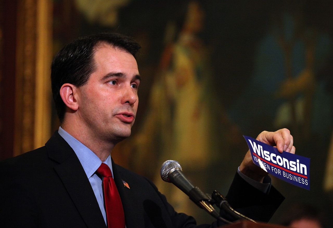 Walker holds up a 'Wisconsin is open for business' bumper sticker as he speaks during a ceremonial bill signing outside his office at the Wisconsin State Capitol on March 11, 2011, in Madison, Wisconsin. 