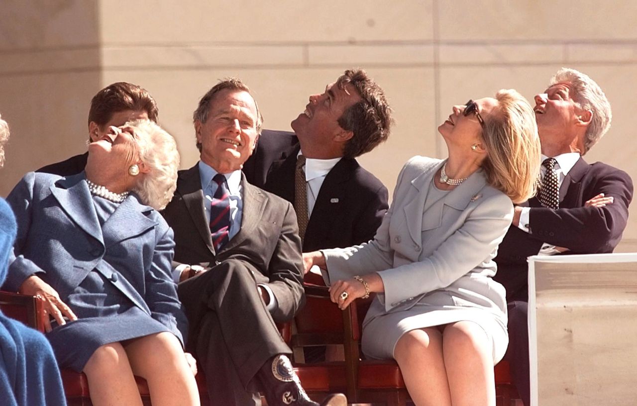 Former President George H.W. Bush (second left), his wife Barbara Bush (left), their son Jeb Bush (center), then-first lady Hillary Clinton (second right), and former then-President Bill Clinton (right) look up to see the U.S. Army Golden Knights parachute team November 6, 1997 at the conclusion of the dedication ceremony of the George Bush Library in College Station, Texas. 