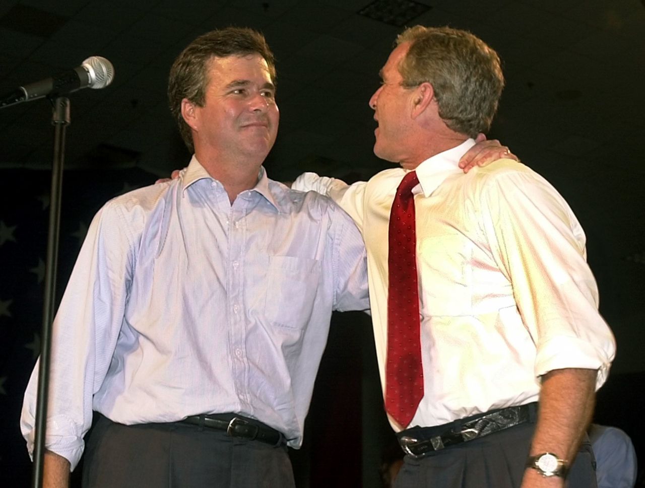 Jeb Bush (left) and then-President George W. Bush stand with their arms around each other's shoulders at a rally in Miami, Florida, September 22, 2000.