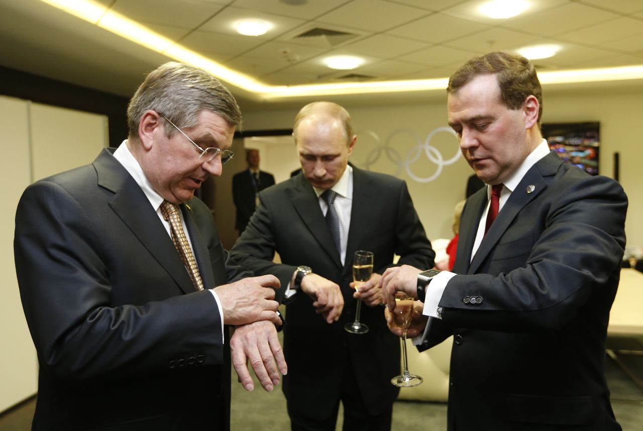 From left, International Olympic Committee President Thomas Bach, Putin and Medvedev look at their watches before the closing ceremony of the Winter Olympics in February 2014.