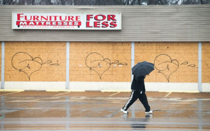 A pedestrian walks past a boarded-up furniture store March 13 in Ferguson. Some businesses in the city haven't reopened since last fall's riots, though a number continue to operate despite being boarded up.