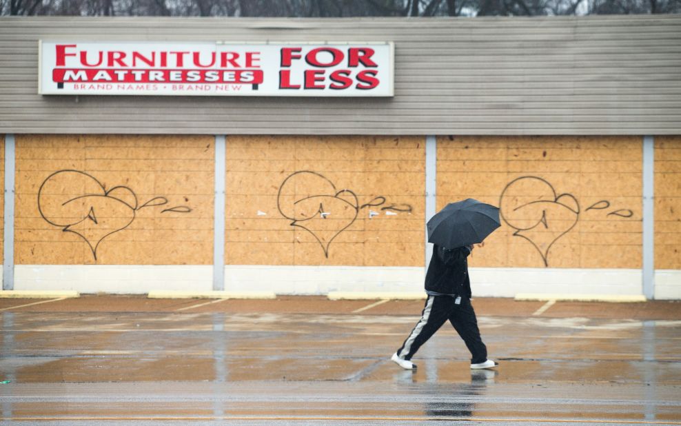A pedestrian walks past a boarded-up furniture store March 13 in Ferguson. Some businesses in the city haven't reopened since last fall's riots, though a number continue to operate despite being boarded up.