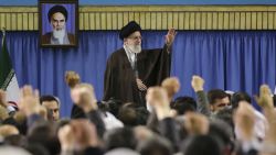 In this picture released by an official website of the office of the Iranian supreme leader, Supreme Leader Ayatollah Ali Khamenei waves while attending a meeting with a group of environmental officials and activists at his residence in Tehran, Iran, Sunday, March 8, 2015. A portrait of the late revolutionary founder Ayatollah Khomeini hangs in background. (AP Photo/Office of the Iranian Supreme Leader)