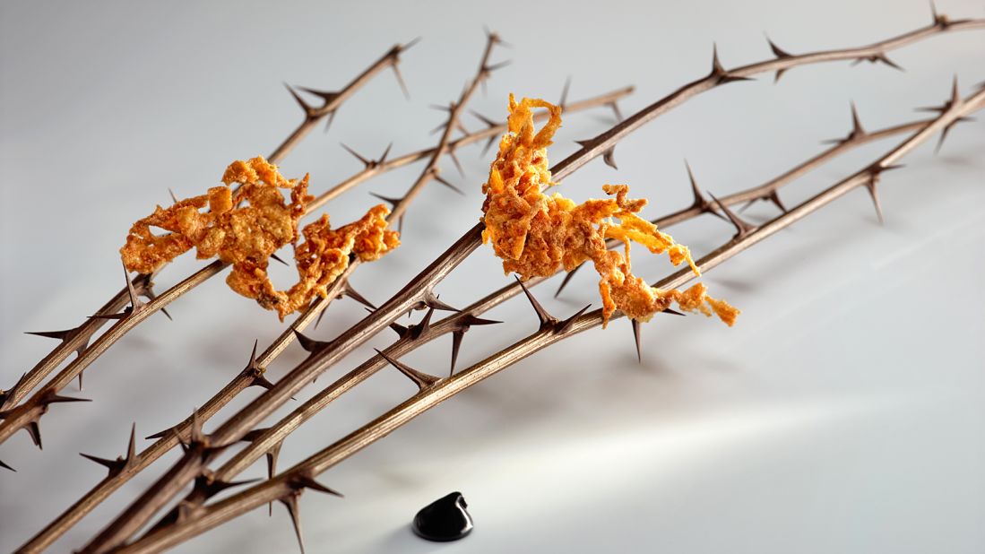 Pieces of fried beef tendon are stretched on thorny branches accompanied by a sweet balsamic dipping sauce of honey mead, egg yolk and ash, which give the dish a black color.