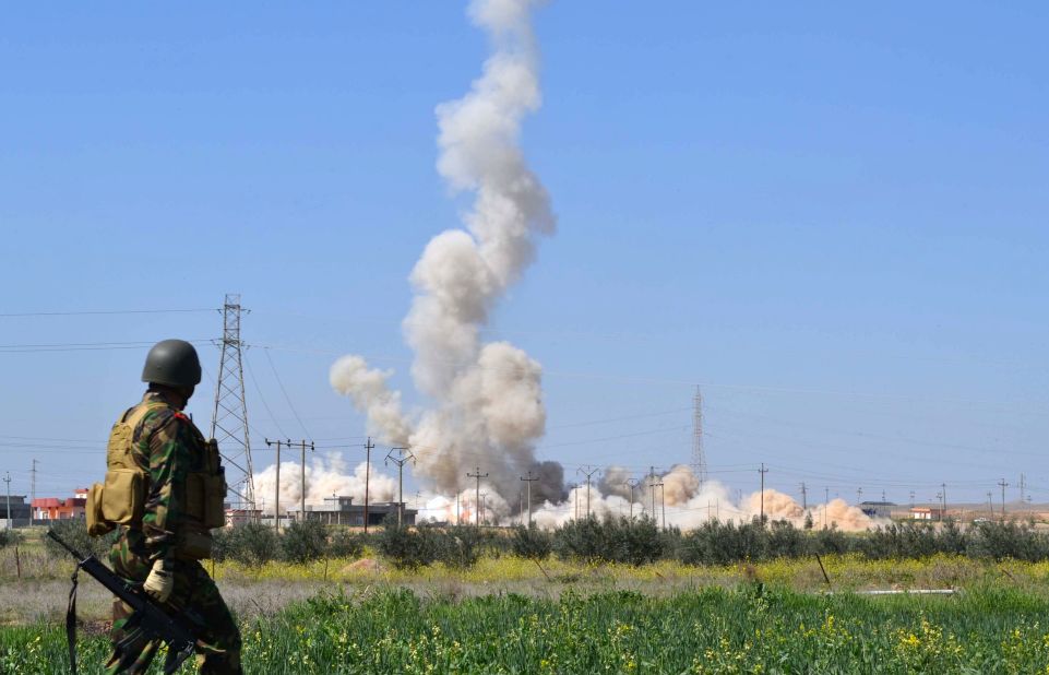 A member of the Kurdish Peshmerga forces looks at a cloud of smoke rising from buildings in a village east of the northern Iraqi city of Kirkuk in March 2015.