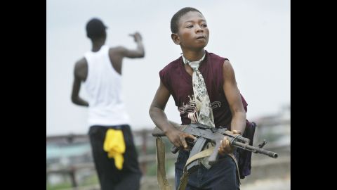  A Liberian militia child loyal to the government walks away from firing on rebel forces across a key bridge while another taunts them in Monrovia in 2003. 