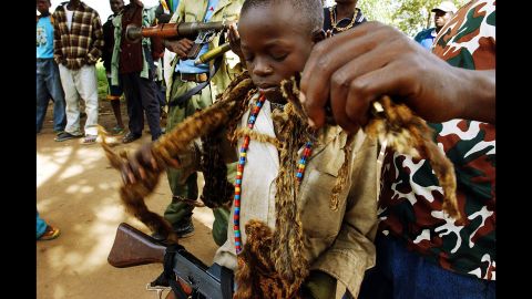 A child soldier is helped by another militiaman as he puts on the traditional chief's hyena skins in an undisclosed location near Bunia in the Democratic Republic of Congo in 2003.