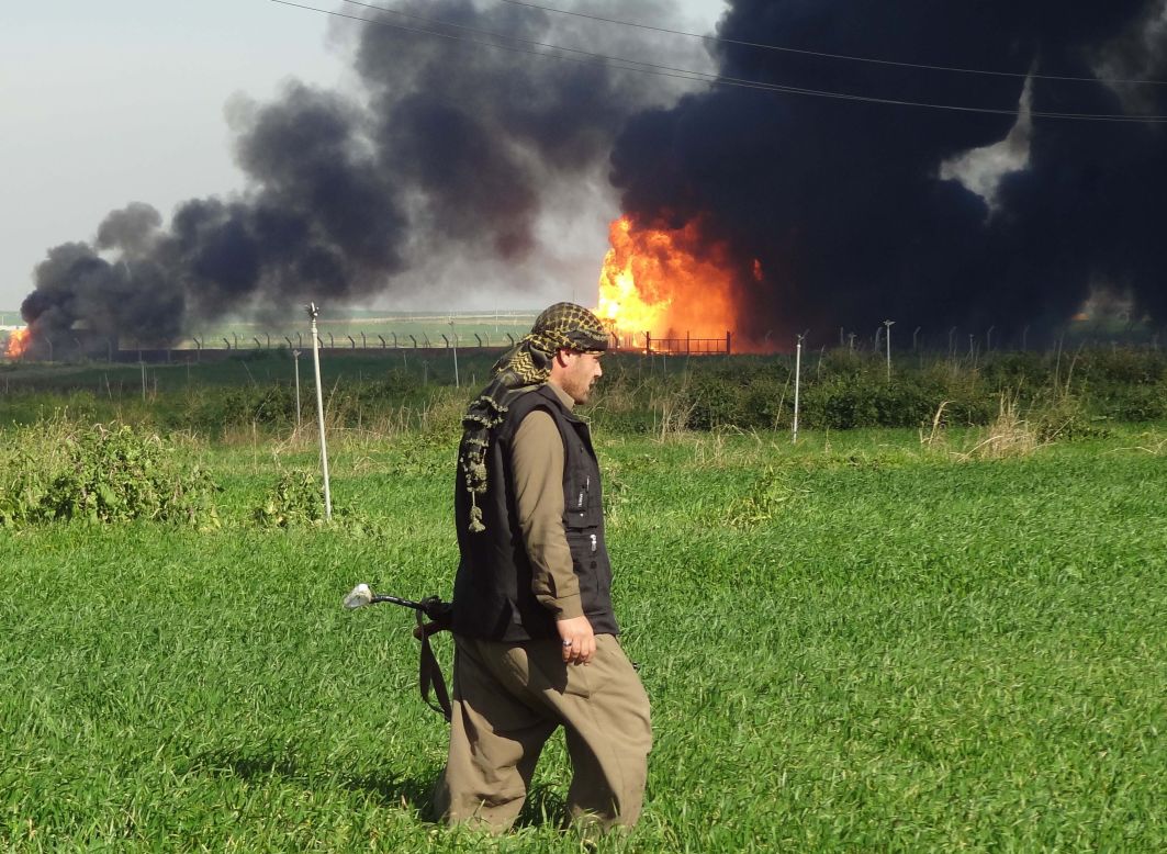 A member of the Kurdish Peshmerga forces walks at the Khubbaz oil field 25 km west of Kirkuk, as smoke billows in the background, in February 2015.