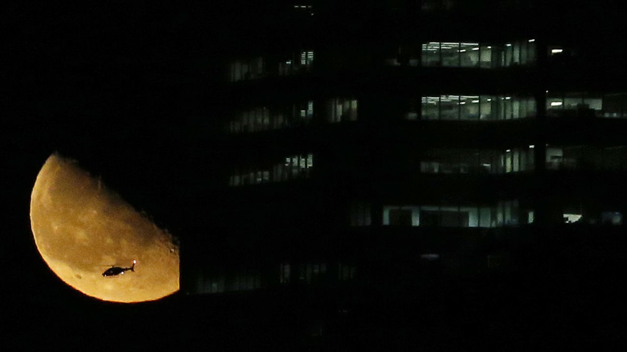 A helicopter flies over New York City as the moon rises near a building on Friday, March 13.