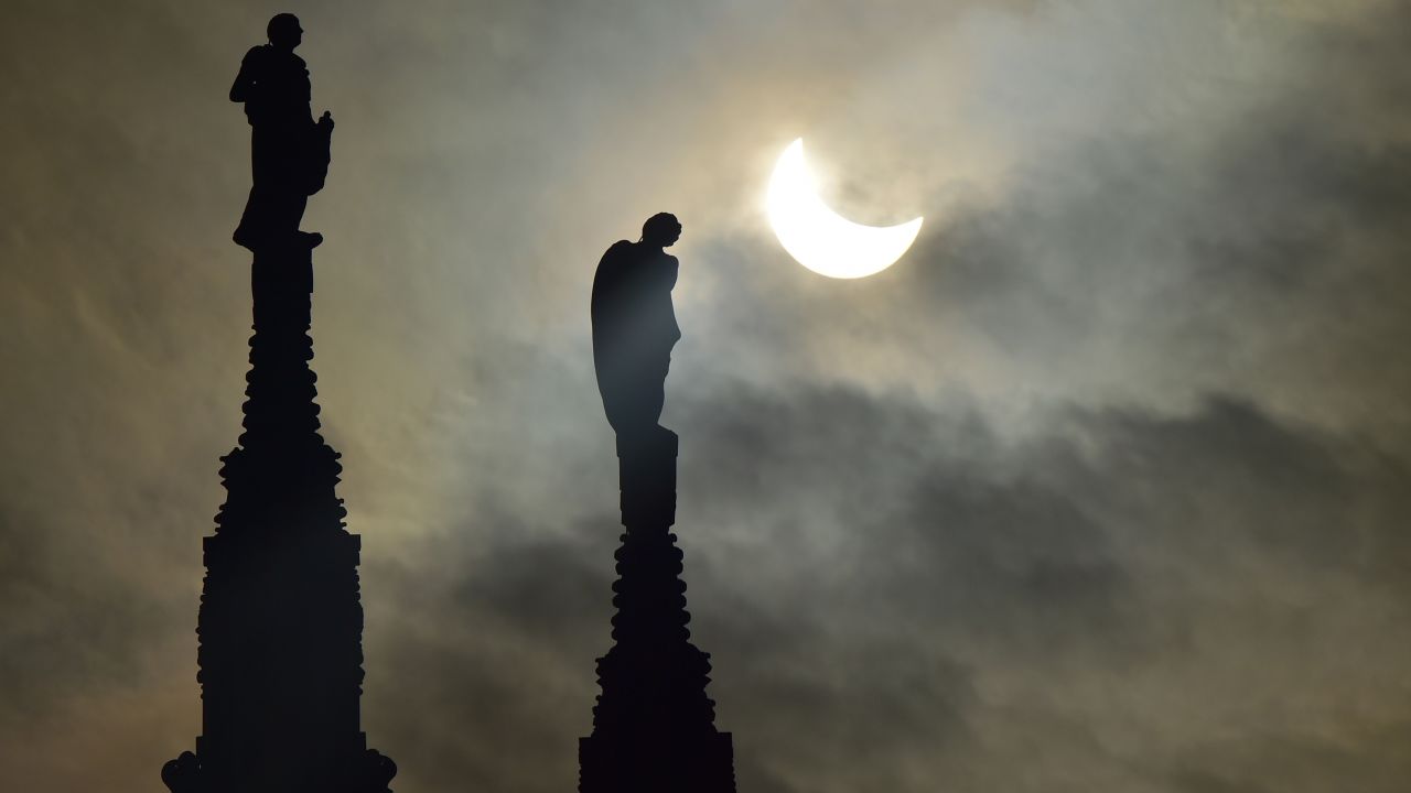 The partial solar eclipse is visible next to cathedral statues in Milan, Italy.