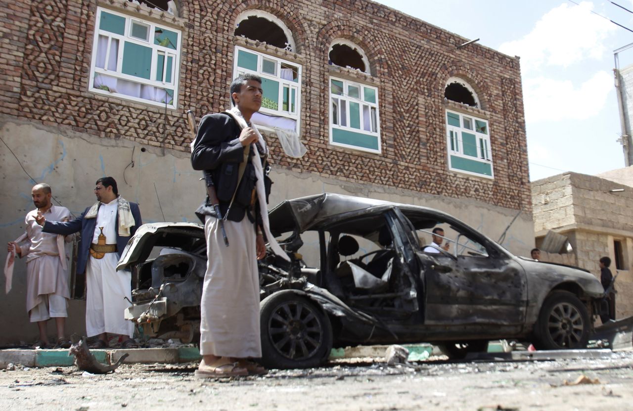 Houthi fighters stand near a damaged car after bombings in Sanaa on March 20. The attacks started with suicide bombings inside the buildings, followed shortly by explosions outside, two senior Houthi leaders said.