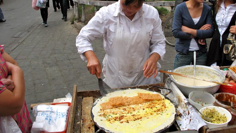 Street chefs ladle batter on a hot pan, swirl it into a perfect circle, then break an egg on top. They can fill the center with anything from deep-fried dough and ham sausages to sweet paste and chili sauce with coriander.