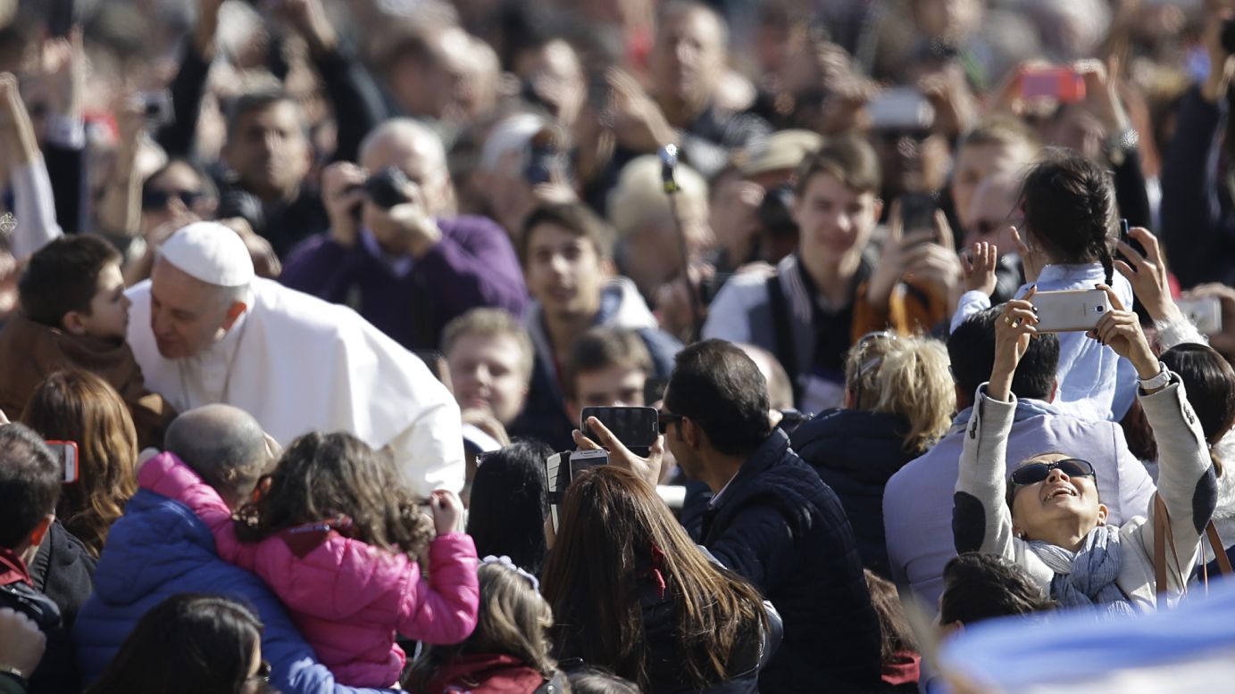 A woman, right, tries to take a selfie with Pope Francis in the background Wednesday, March 18, in Vatican City.