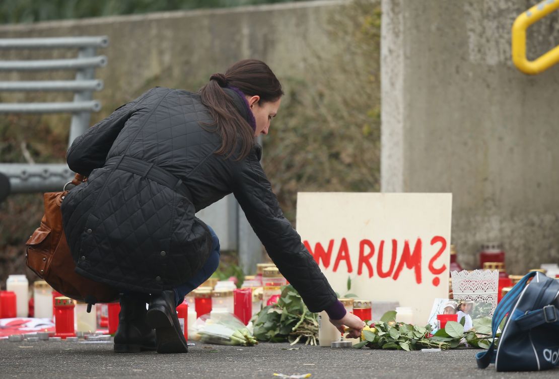 A woman lights a candle next to a sign reading: 'Why?' at the Joseph-Koenig-Gymnasium in Haltern, Germany.