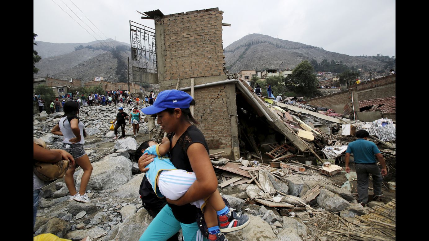 A woman carries a baby Tuesday, March 24, as she walks past homes that were destroyed by a massive landslide in Chosica, Peru.