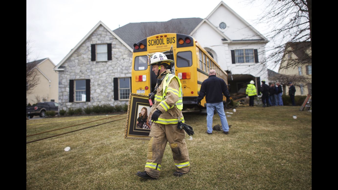 A firefighter removes a family portrait from a house that was crashed into by a school bus Tuesday, March 24, in Blue Bell, Pennsylvania. No injuries were reported, police said.