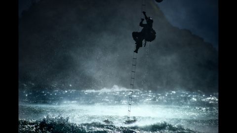 A 22nd Special Tactics Squadron airman climbs a ladder into a CH-47 Chinook helicopter hovering over the ocean on June 20, 2014. 