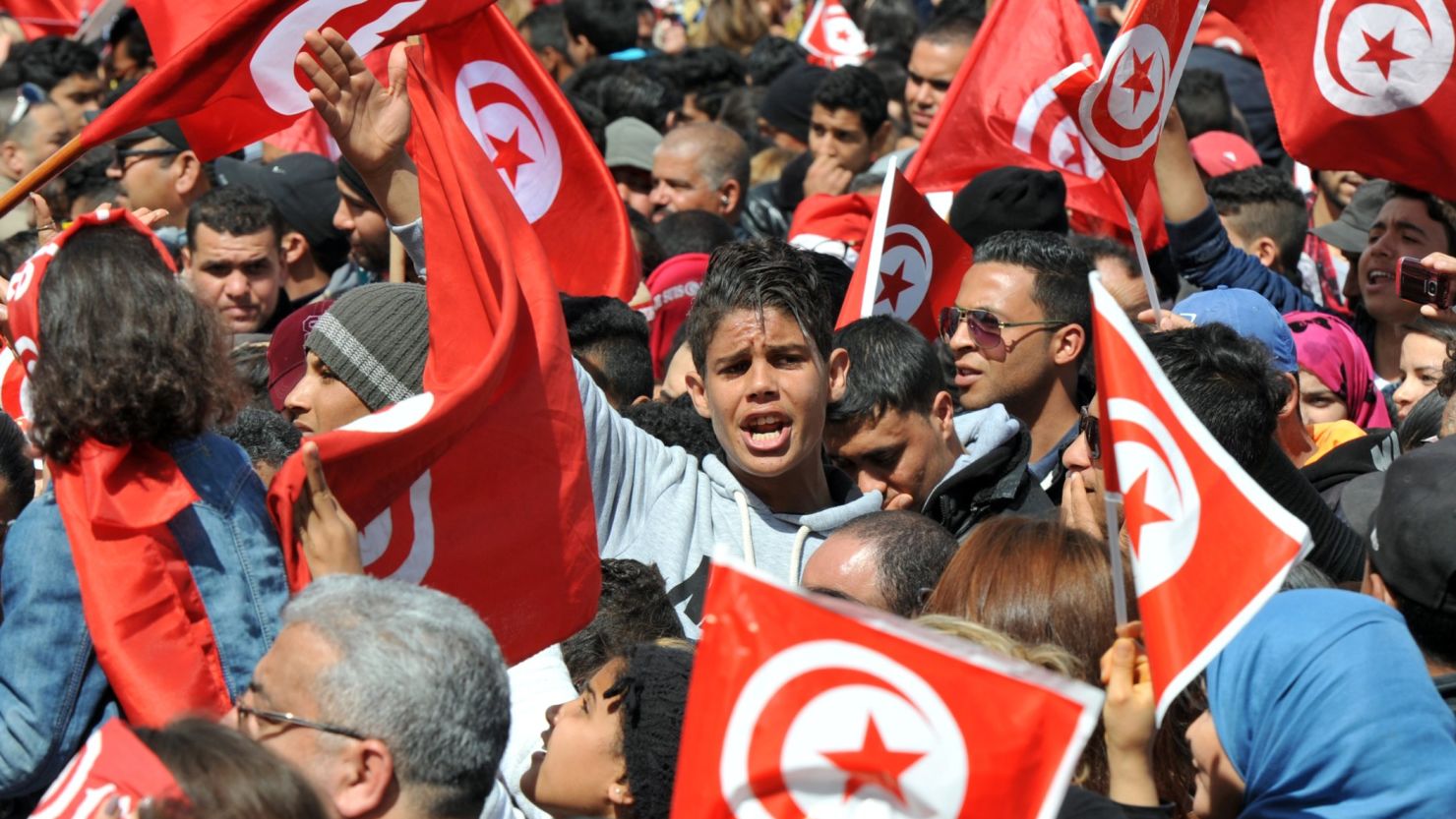Tunisians wave their national flag and chant slogans during a protest against terrorism outside the Bardo Museum in Tunis on March 29, 2015.