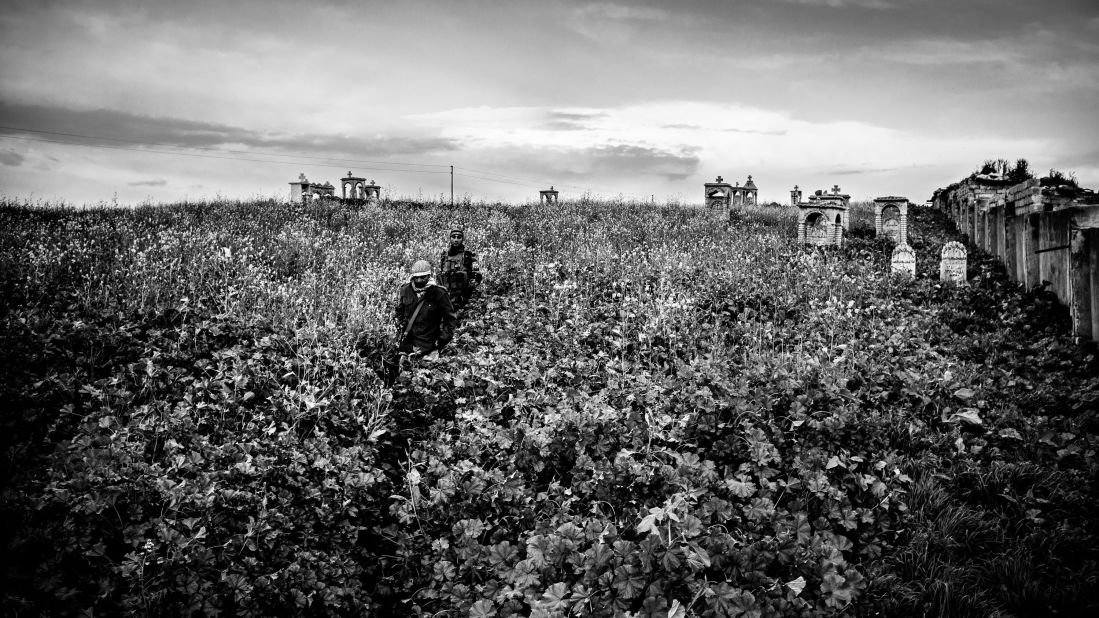 Dwekh Nawsha fighters walk through a Christian cemetery in Baqufa.