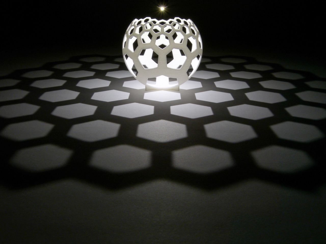 Light shone from a pinpoint source creates a "map" on the table in the shadow of the globe. A grid of straight lines appear from the curved 3D-printed sculpture. 