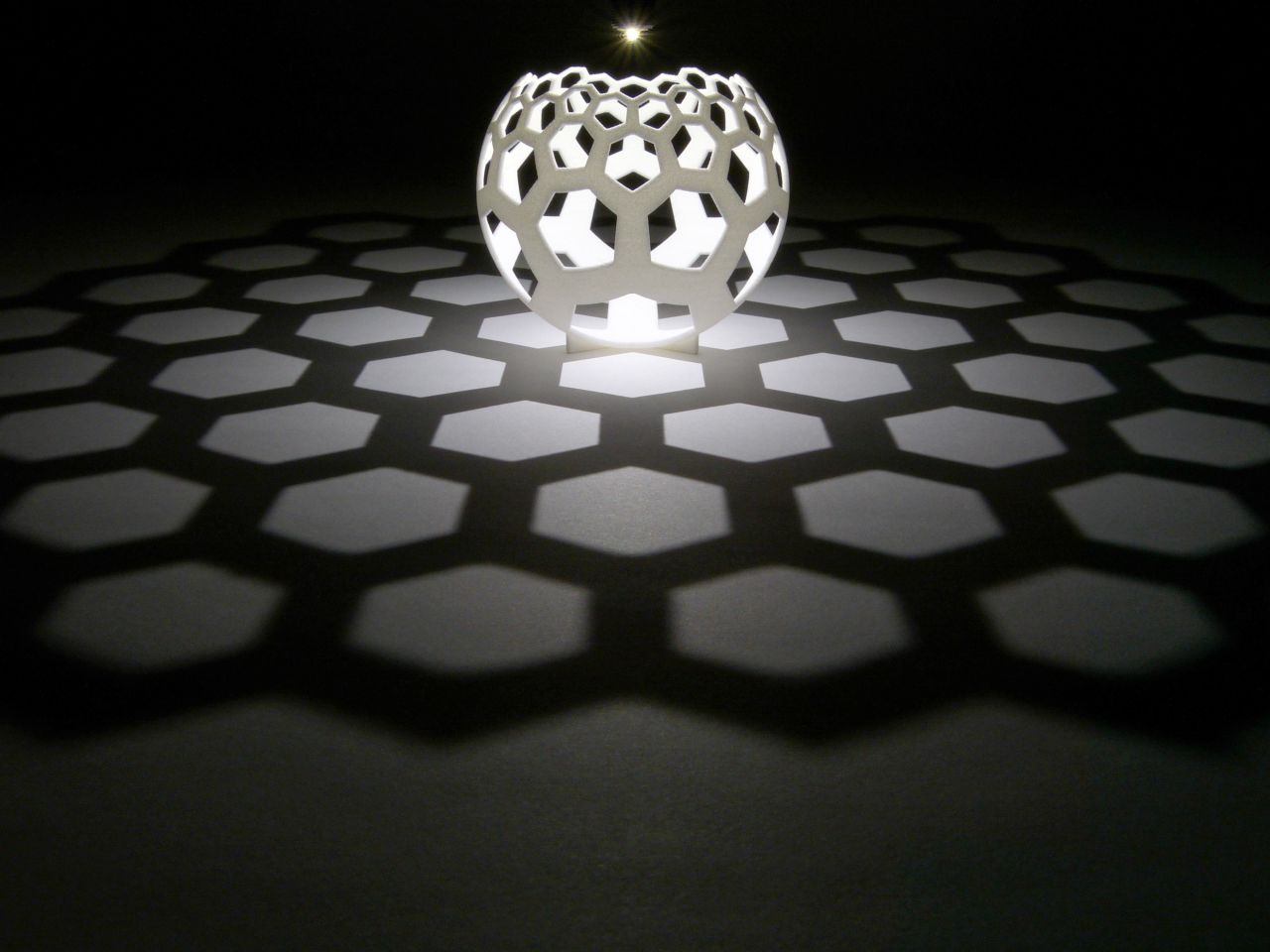 Light shone from a pinpoint source creates a "map" on the table in the shadow of the globe. A grid of straight lines appear from the curved 3D-printed sculpture.