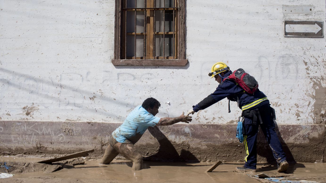 A rescue worker stretches his hand to help a local resident cross a mud-covered street in Chanaral, Chile, on Friday, March 27. Heavy thunderstorms, torrential rains and overflowing rivers left tons of mud in parts of northern Chile.