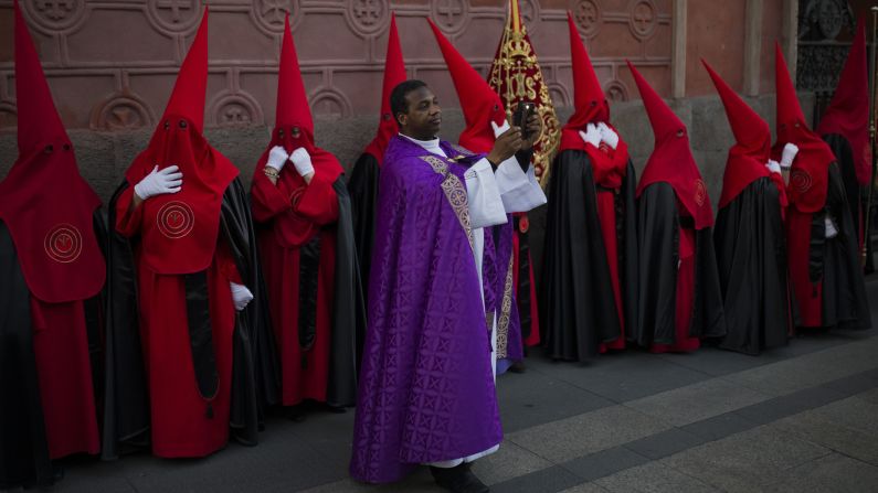 A priest takes a photo as penitents stand during a procession of  "La Soledad" in Madrid, Spain, on April 4. Hundreds of such processions take place throughout Spain.