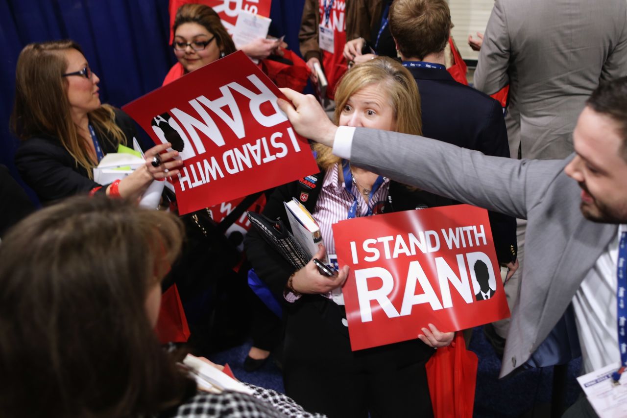 Paul supporters are handed placards reading "I Stand with Rand" while waiting in line for a book signing with the senator at the Conservative Political Action Conference.
