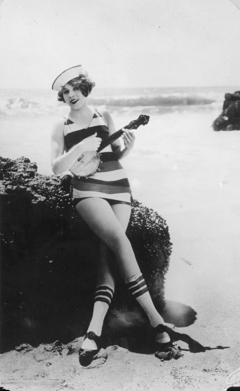 The sailor suit is re-imagined as swim wear in this 1923 image of a girl playing a banjo on the beach.