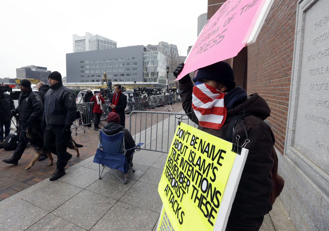 Protestor Jose Briceno holds signs outside court denouncing Tsarnaev, his face covered by a U.S. flag.