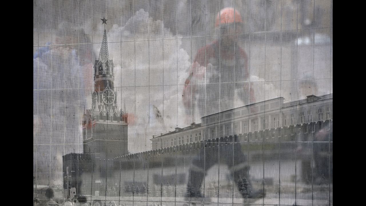 A worker in Moscow walks behind a transparent fence bearing an image of Red Square at a construction site outside the Kremlin on Tuesday, April 7.