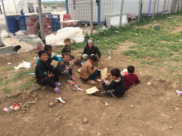 Children play in the dirt with toys crafted from cardboard. Some clamber through the wire fence and play with rocks -- anything to keep themselves entertained.