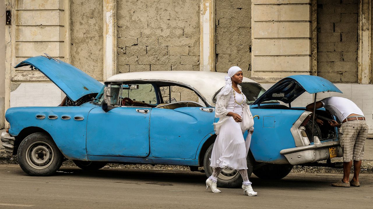 A woman walks past a vintage American car on December 31, 2013, in Havana. A new regulation released by Cuban President Raul Castro will allow Cubans or foreign residents to freely buy new or used cars in government-run stores as of January 3, 2014; after 50 years of automobile sales regulations.