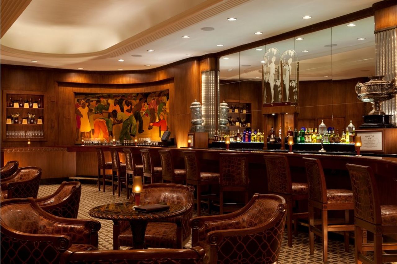 Famous Paul Ninas murals flank the curvaceous walnut-paneled room, furnished with elegant bar stools and plush banquettes. 
